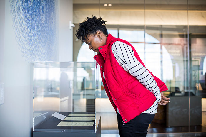 A member of the Emory community in a red vest looks at the original letters on display in a glass case.