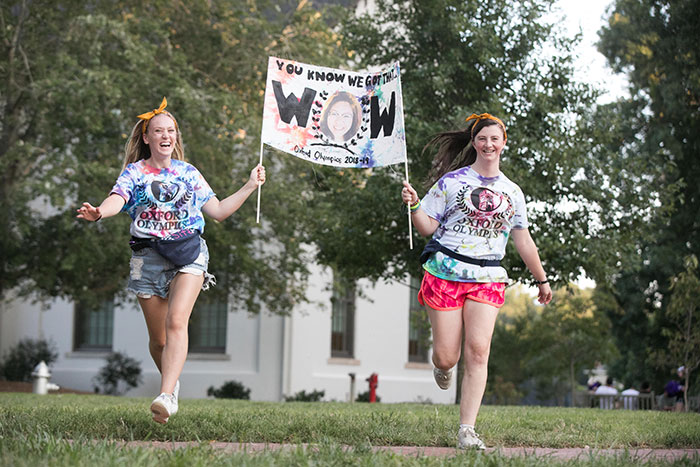 Two students run through the quad carrying a sign for the team