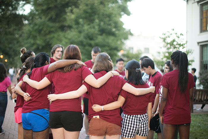 Students wearing maroon t-shirts wrap their arms around each other in a huddle