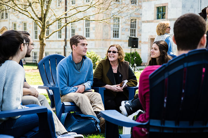Emory President Claire E. Sterk kneels between two students, smiling as she speaks to them at Conversations on the Quad