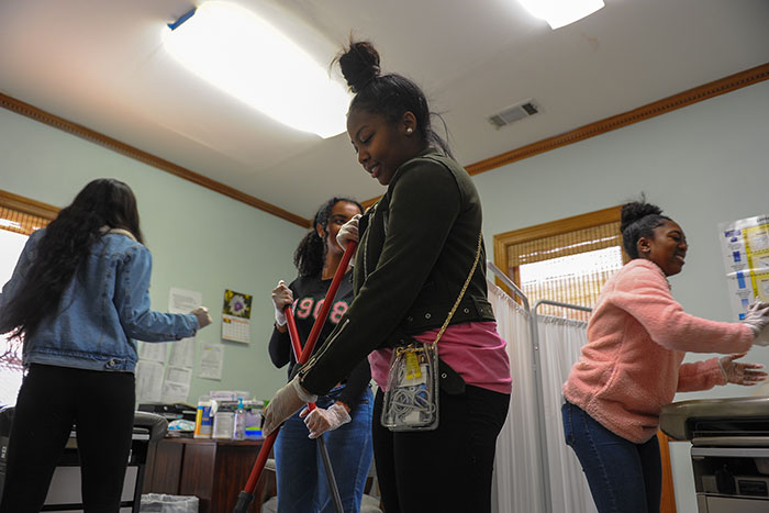 Students use brooms and mops as they help clean at Harriet Tubman Women's Clinic