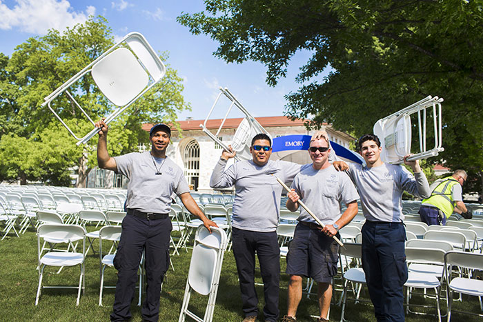 Four Emory employees hold folding chairs high in the air as they work on setting them up