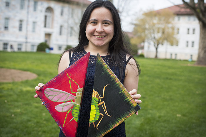 Pamela Romero holds her artwork up for the camera. The DNA painted along the edges of the canvases is the same, except that different genes are switched on, showing how aphids can develop wings in response to environmental change.