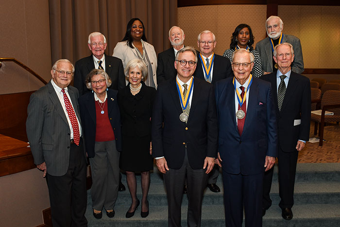 David Adelman and Richard Hubert wear an Emory Medal in the foreground while ten previous recipients stand behind them.