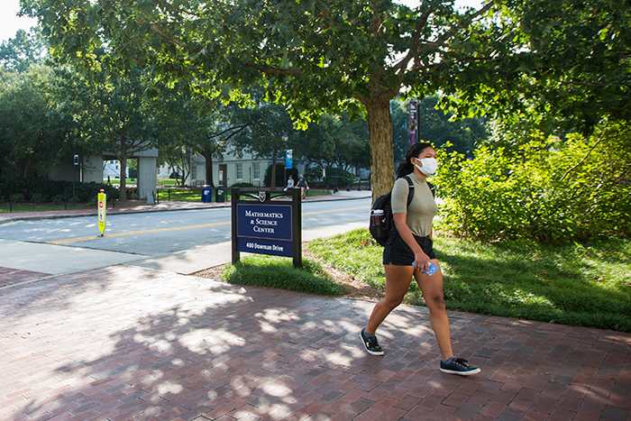 A student walks on campus wearing a mask