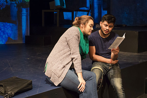 Two people sitting on the edge of a theater stage, reviewing the script