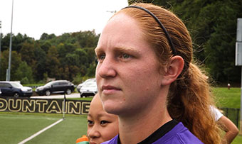 A female soccer player stands on a soccer field