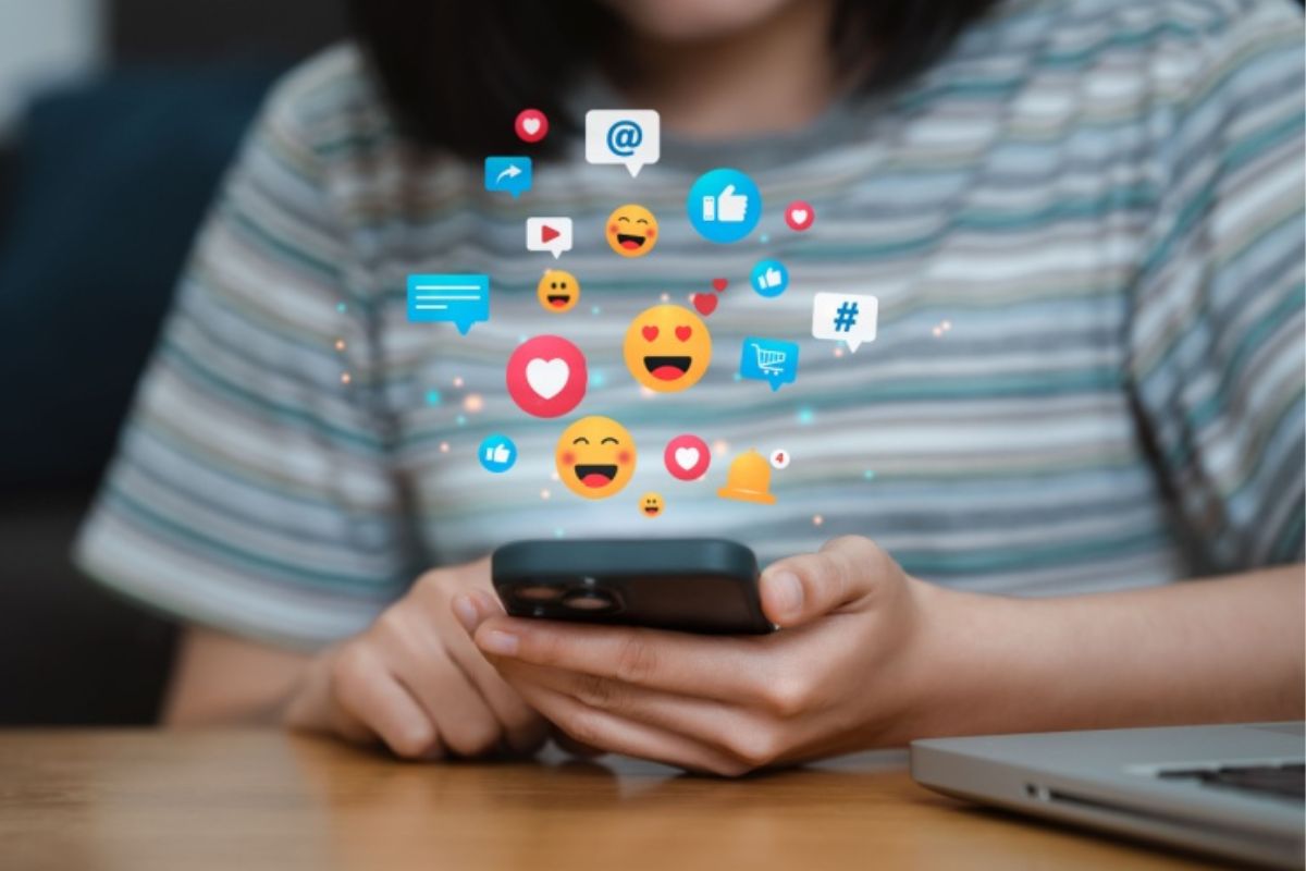 Stock photo of a young person holding their phone with emojis