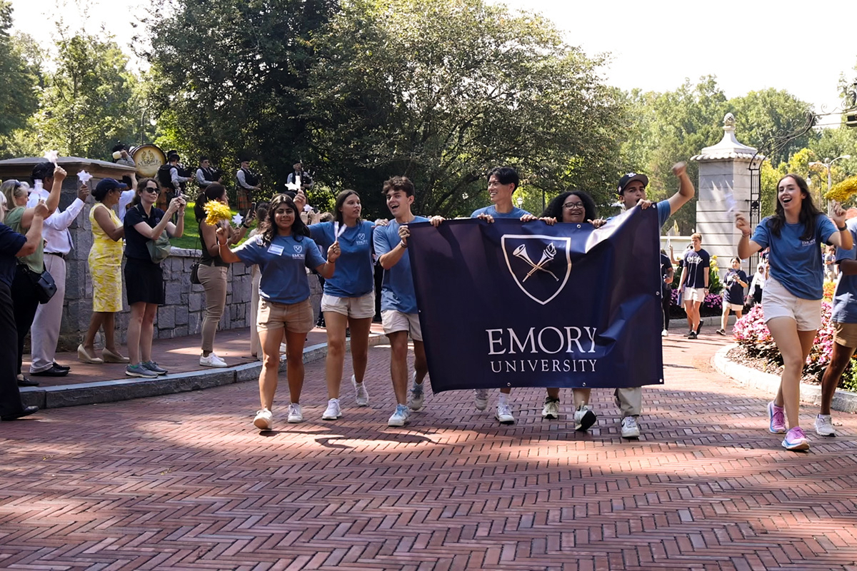 People cheer while Emory University students walk through the campus gate 