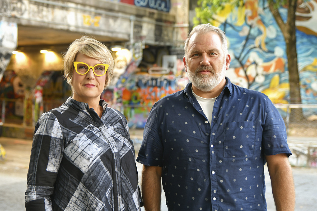 close photo of man and woman standing with colorful graffiti art painted in background