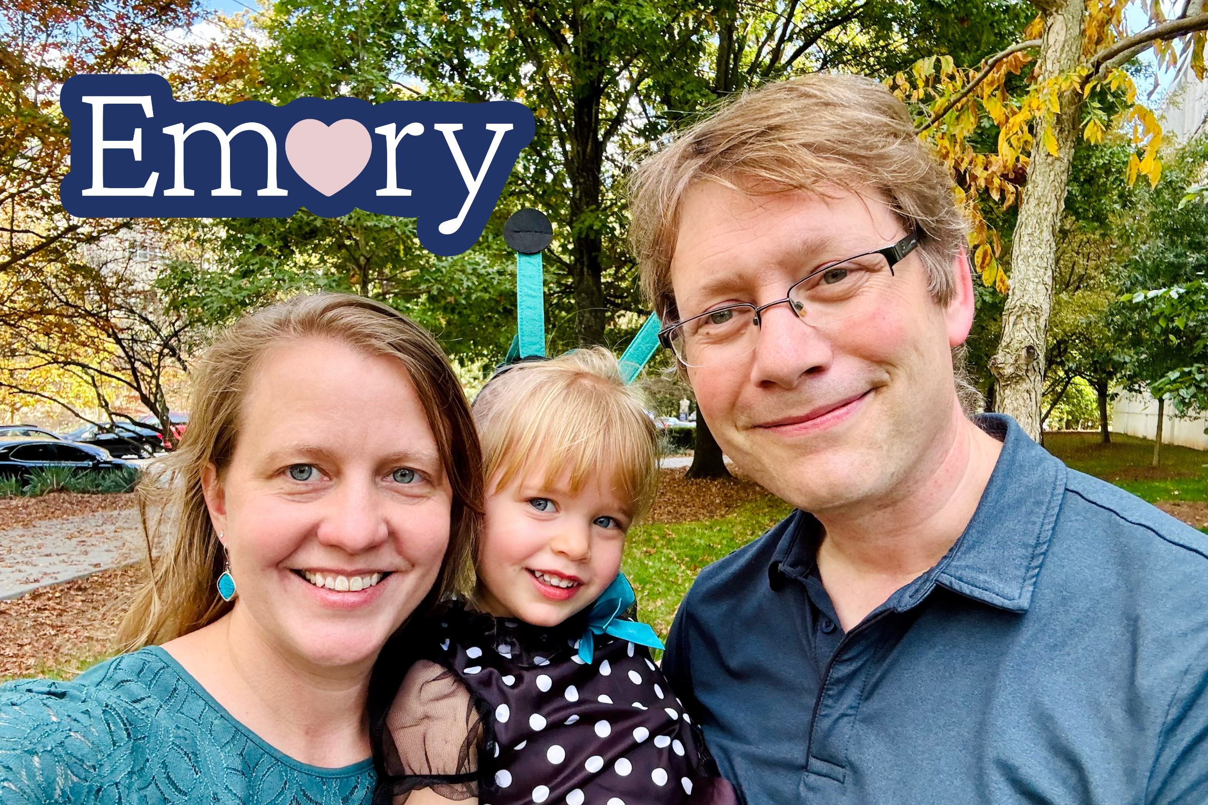 A portrait of an Emory couple holding a toddler daughter, with a sticker that says "Emory" and has a heart