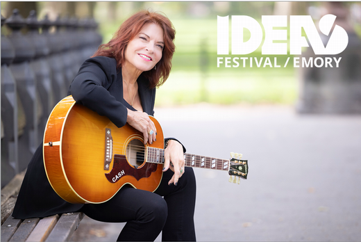 Rosanne Cash sitting on bench outdoors holding her guitar