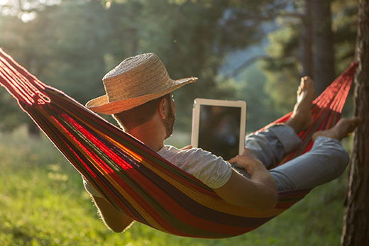 Man in a straw hat using an e-reader in a hammock