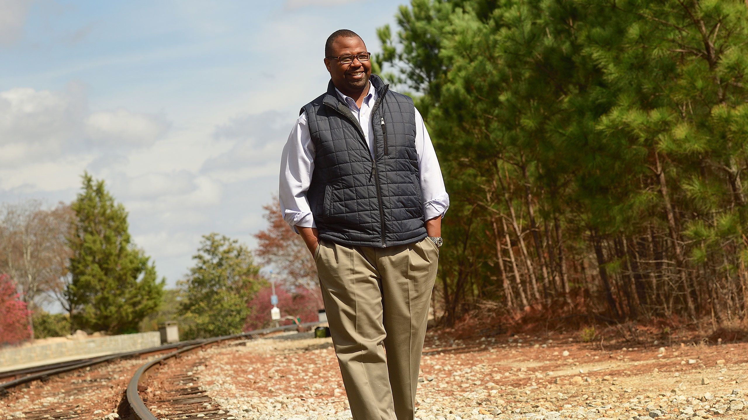 Bradley Carthon walks along railroad tracks surround by trees.