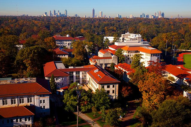 An aerial photo shows the Emory campus surrounded by trees with the Atlanta skyline on the horizon.