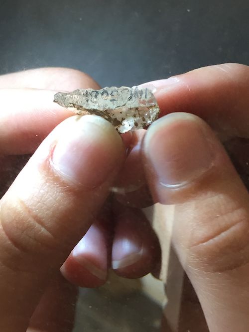 A close-up photo shows a student's fingers holding a small fragment of rock.