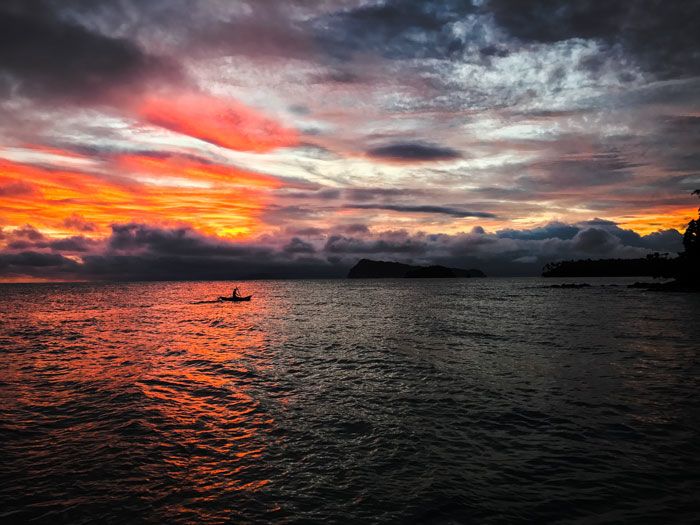 A man in a small boat is silhouetted against an orange and blue sunset in Samoa.