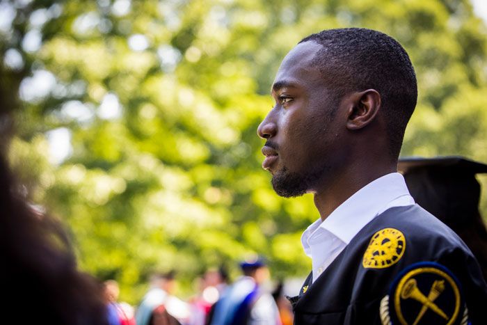 A young man is photographed in profile wearing a graduation gown.