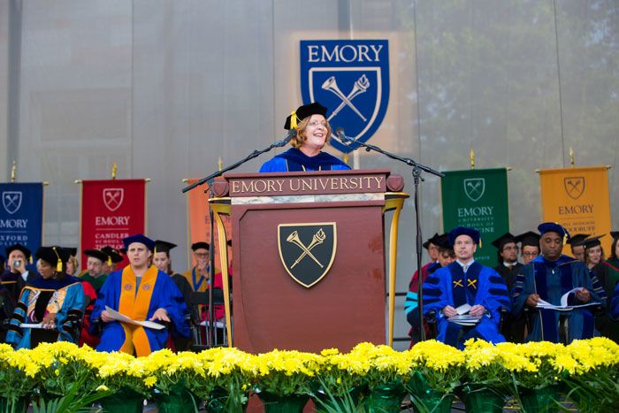 Wearing academic regalia, Emory University President Claire E. Sterk stands at a podium on the Commencement stage.