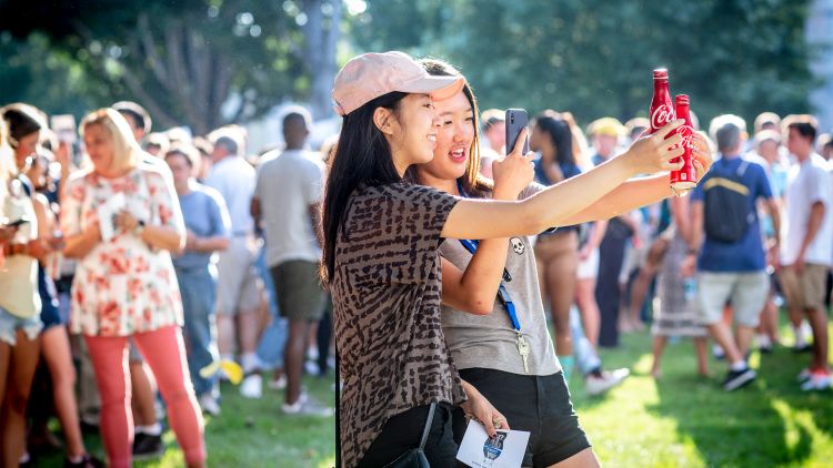 Two students take a photo of their hands holding Coke cans at Emory's Coca-Cola Toast.