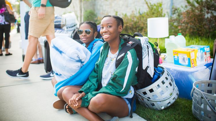 Students sit on the sidewalk with baskets of items on Move-In Day on the Emory campus.