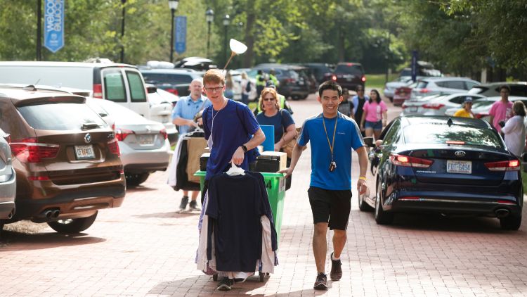 Students carry clothes on hangers and push a cart filled with belongings on the street on the Oxford campus.