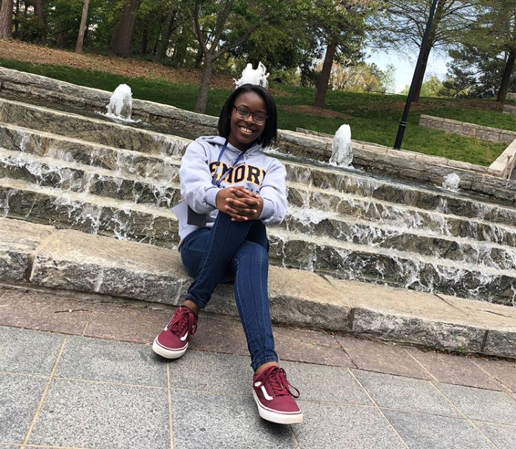 Wearing an Emory gray sweatshirt and jeans, Breona Minefee poses in front of a fountain.