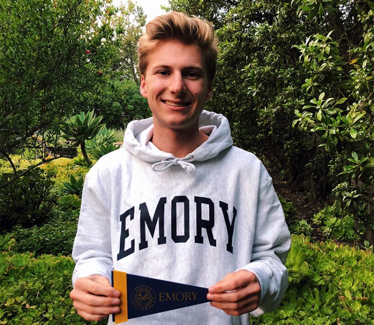 Jason Tayer poses wearing a white Emory sweatshirt and holding an Emory pennant.