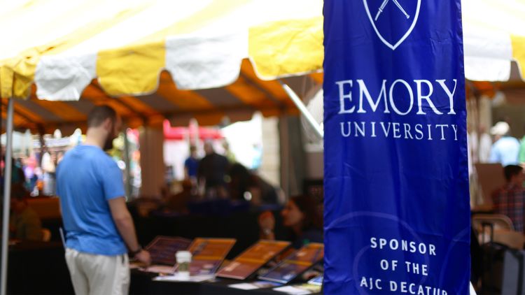 A man stands at a table by the Emory tent at the Decatur Book Festival. A blue Emory University banner is in the foreground.