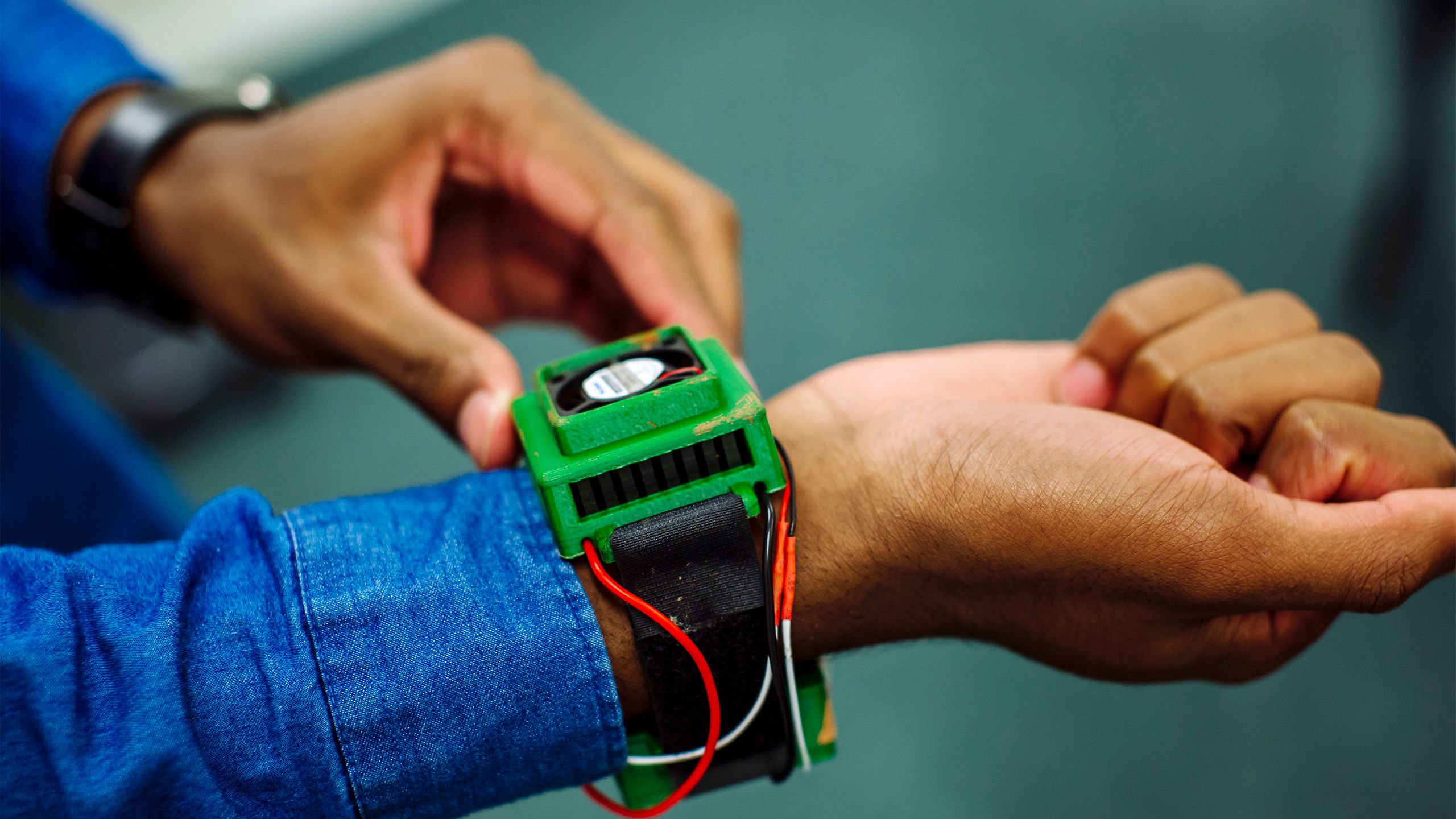 Ryan James wears the Vimband protype. It is a black band with a green electronic unit connected by red and white wires.