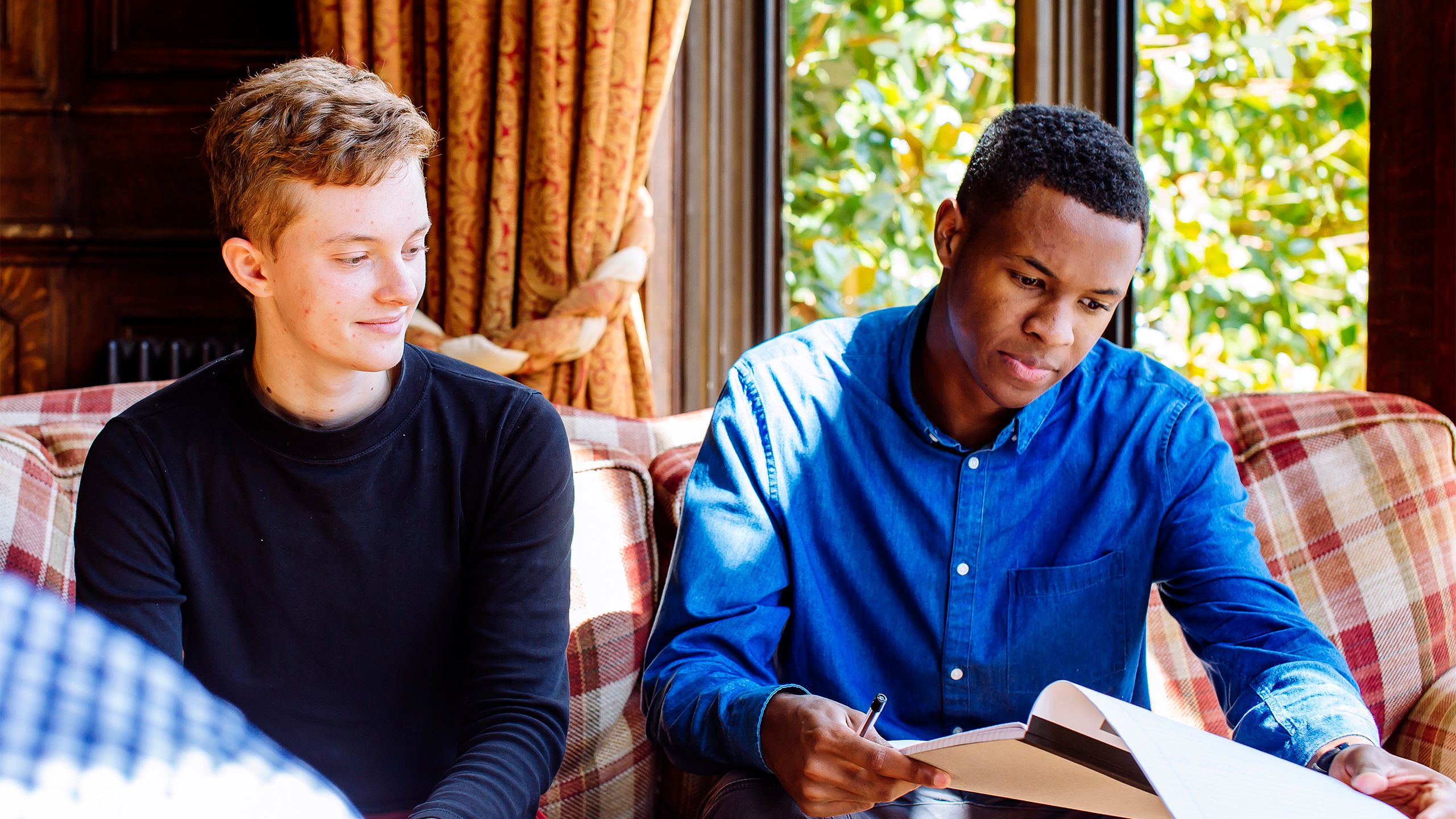 Jesse Rosen-Gooding and Ryan James sit on a plaid sofa and look over notes related to their Vimband project.