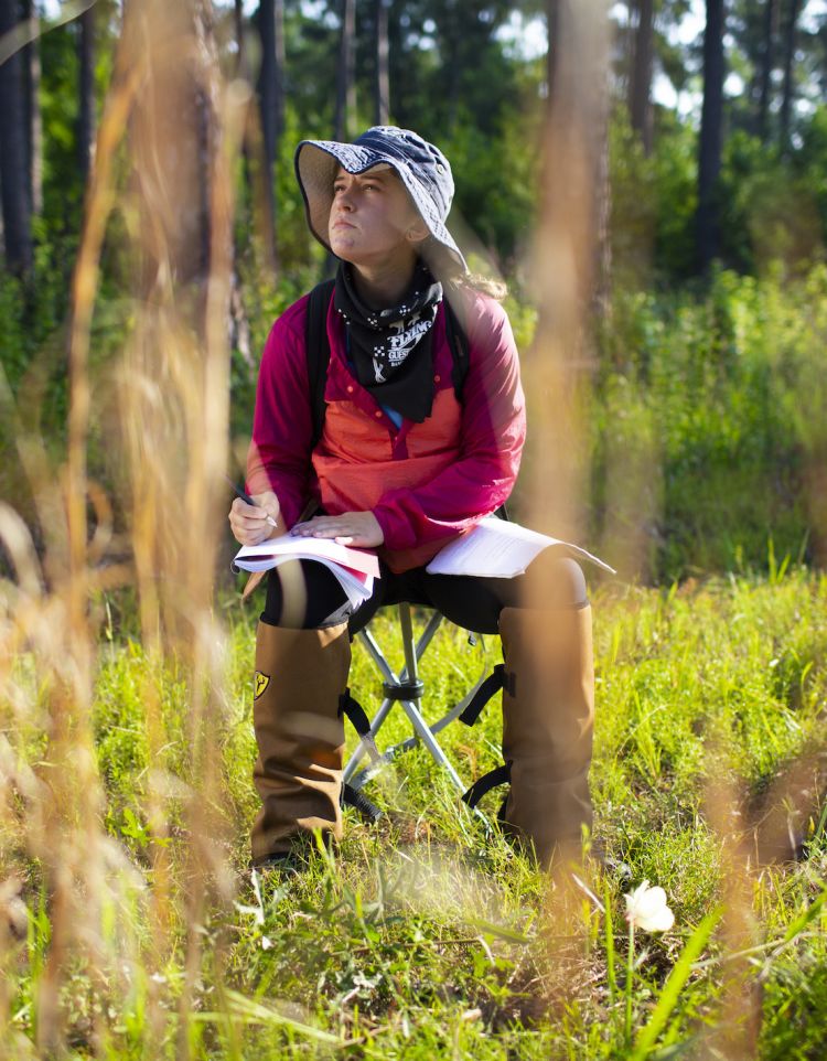 Annie Schiffer sits on a collapsible stool in the forest