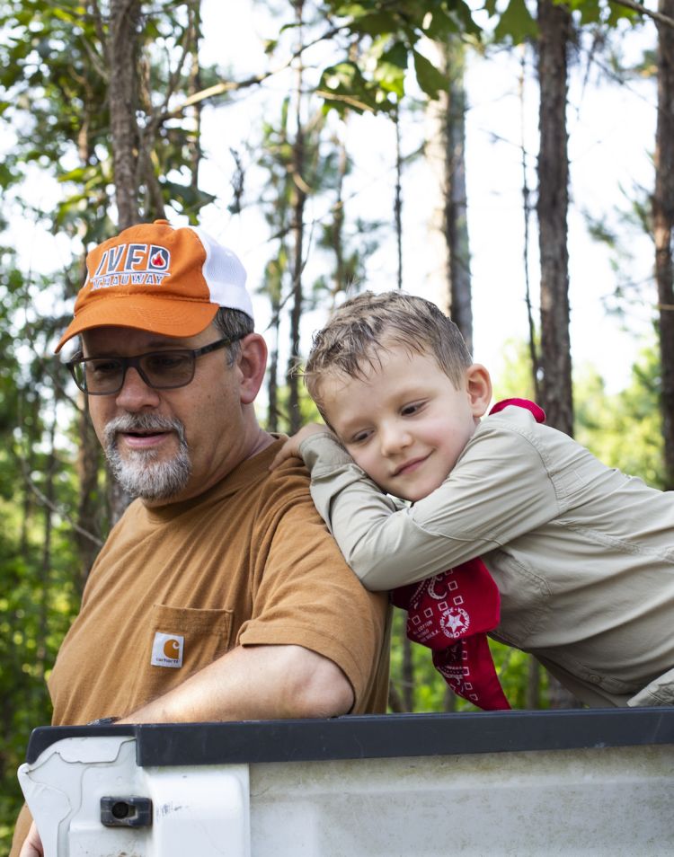 Giacomo, age 5, leans on the shoulder of Kier Klepzig, who is leaning against a pickup truck