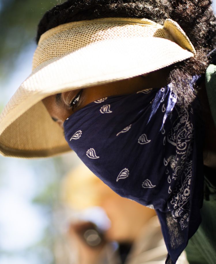 A close up view shows Kat Bagger wearing a sun visor and a blue bandana covering the lower half of her face