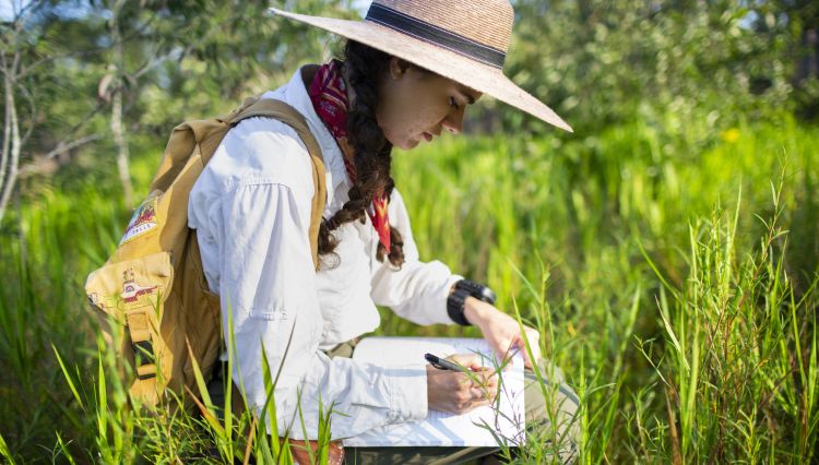 Ella Vardeman sits in the grass writing in a journal