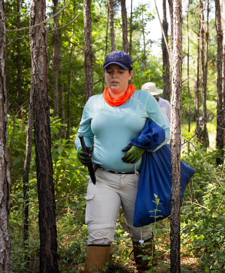Monique Salazar walks through the forest carrying tools and a blue bag.