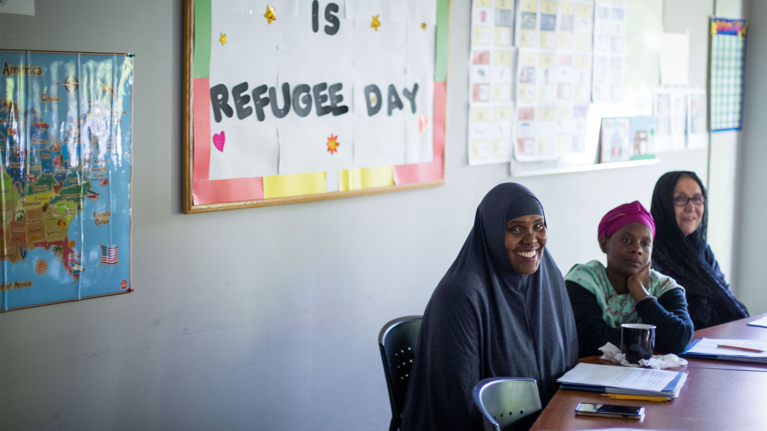 Three women wearing head scarves sit at a table during a class provided by the International Rescue Committee.
