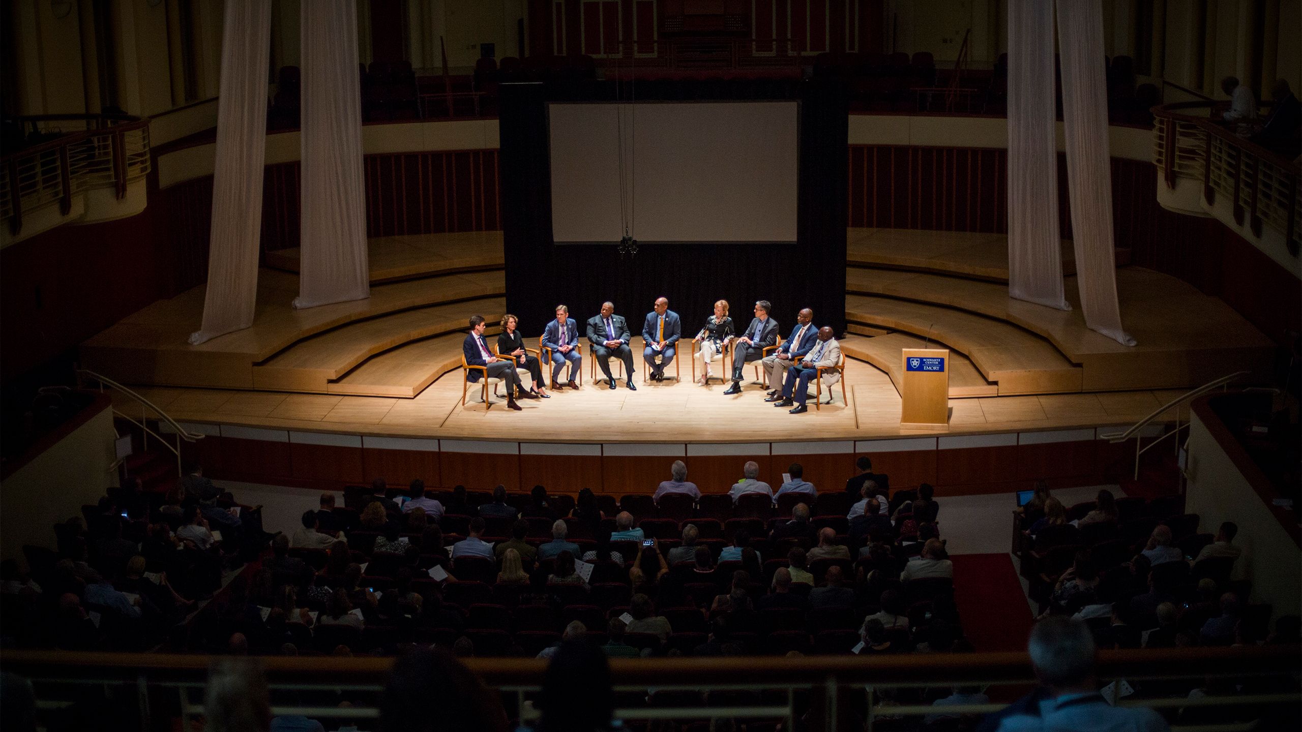 Eight Emory faculty and Provost McBride sit in a half-circle of chairs on the stage of the Schwartz Center for Performing Arts.