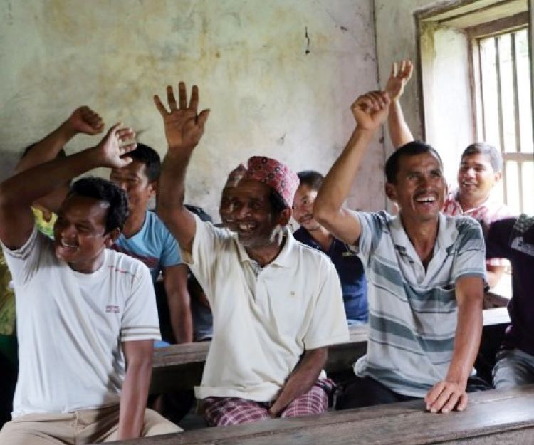 A group of Nepali men in a classroom, smiling, most with their hands raised.