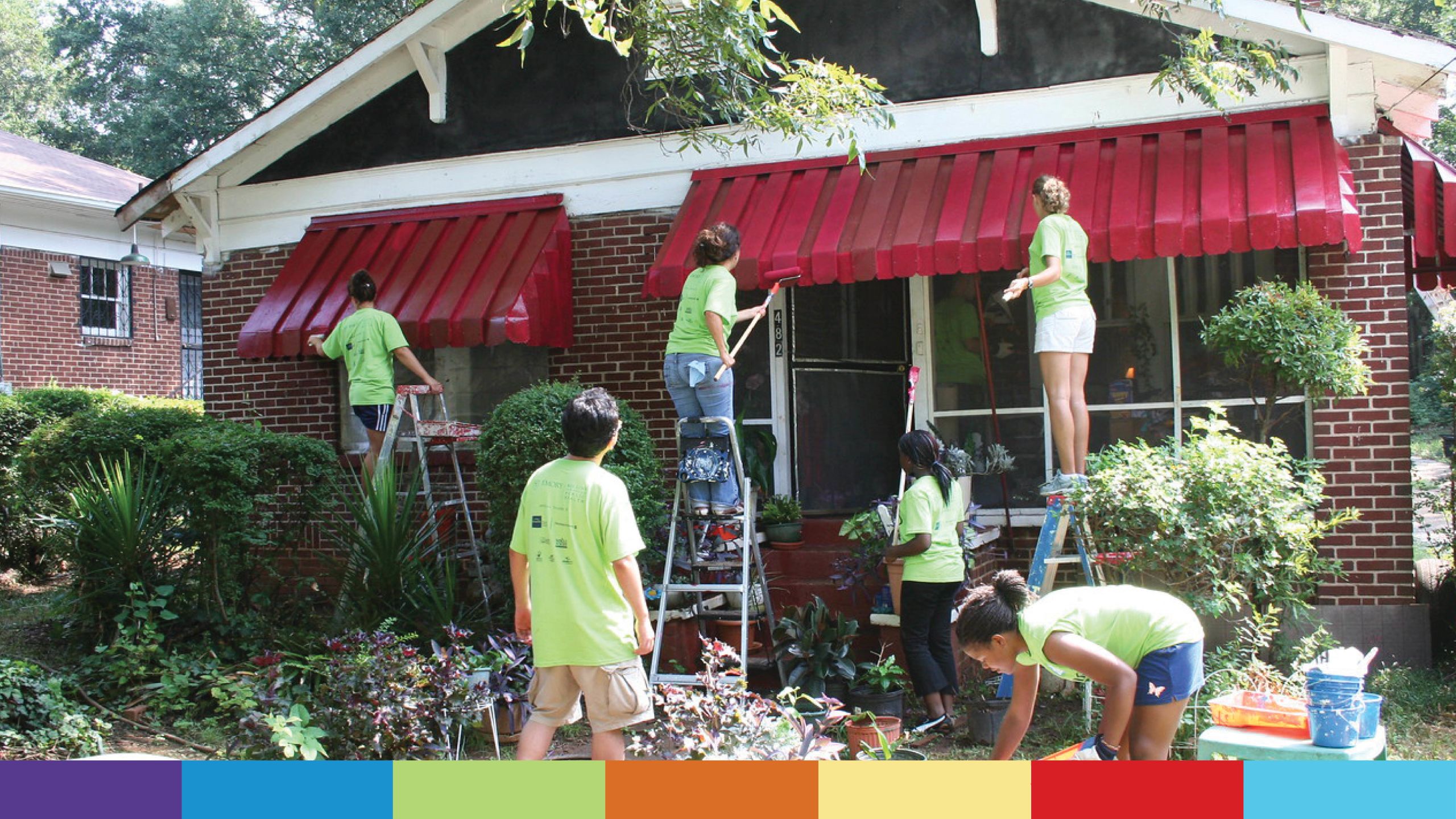 Students in green T-shirts paint a home.