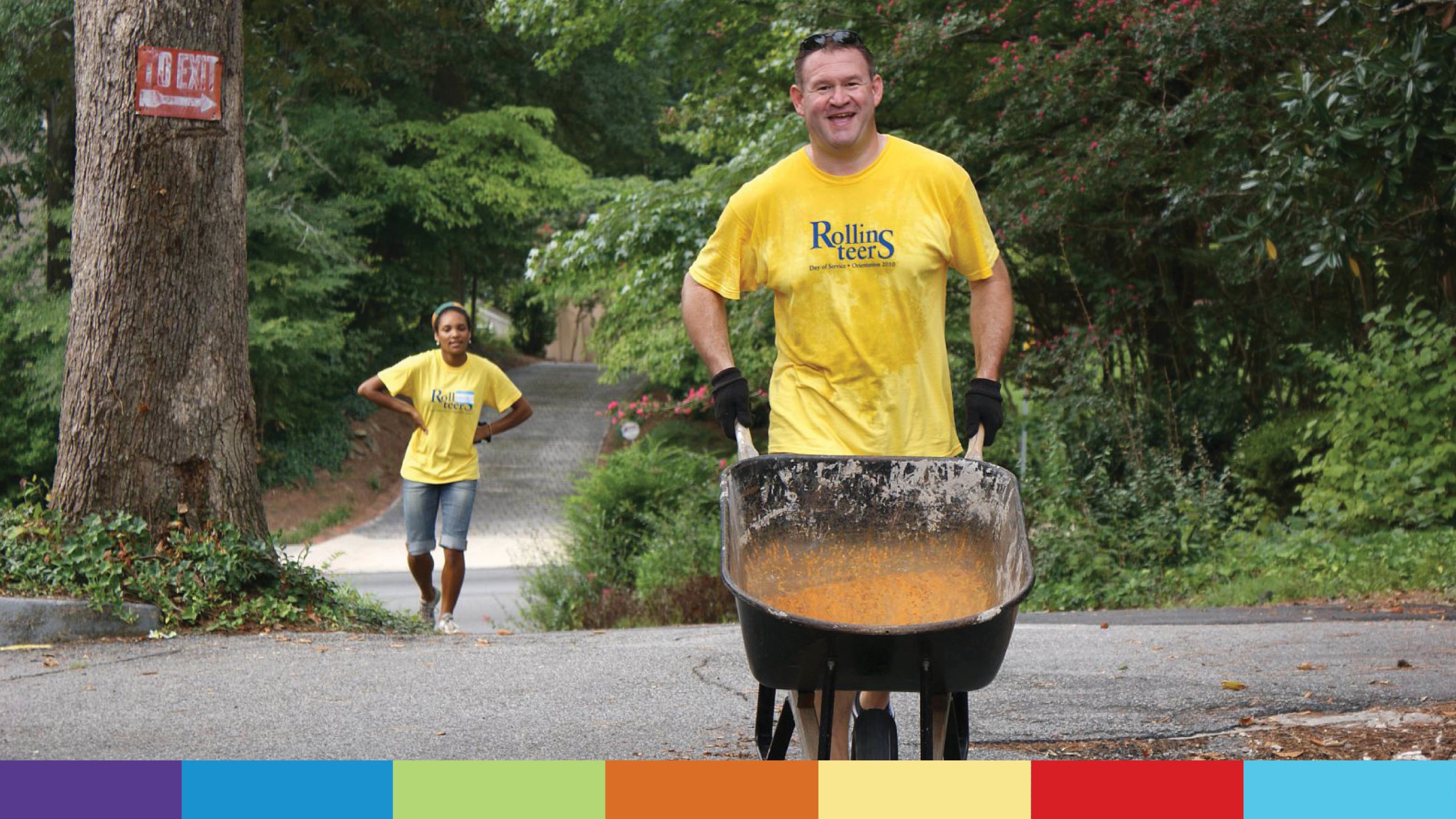 A Rollin-teer in a yellow T-shirt pushes a wheel barrel 