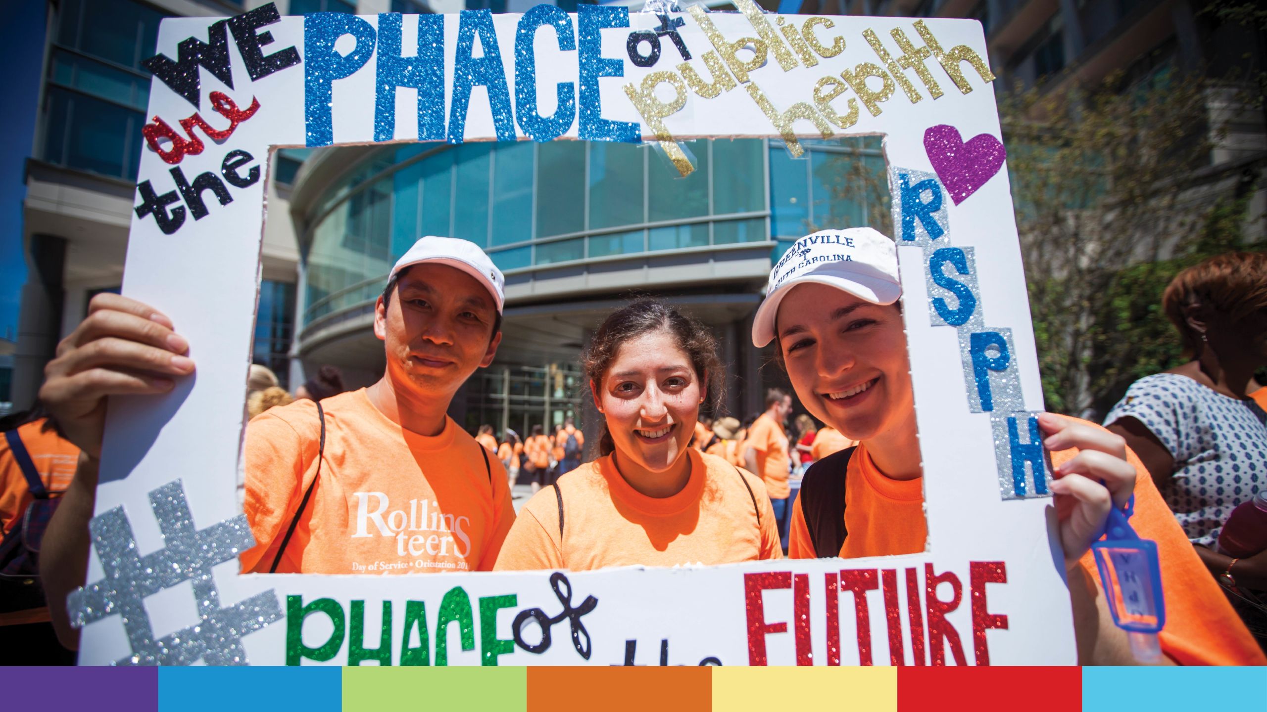 Three volunteers in orange T-shirts pose behind a frame that reads "We are the face of public health"