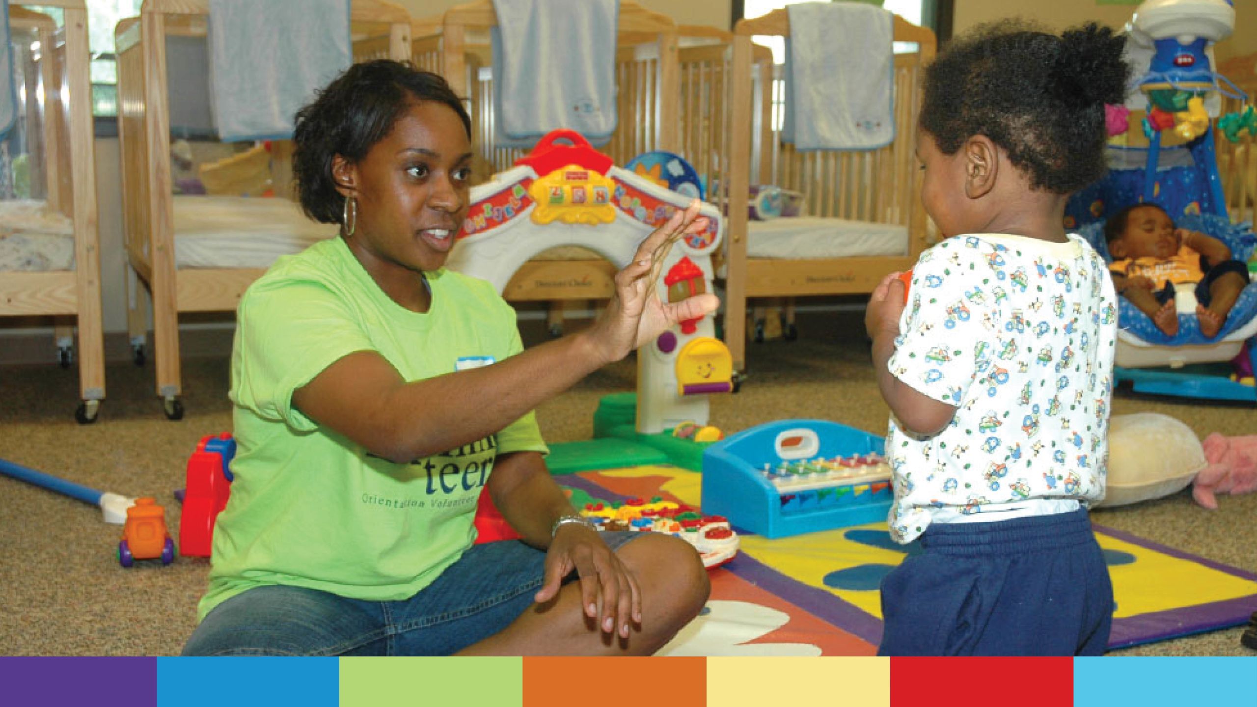 A volunteer in a green T-shirt plays with a toddler in a day care.