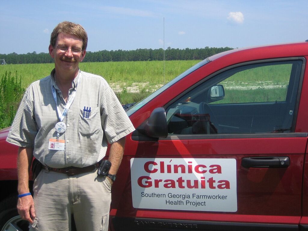 Tom Himelick poses next to his truck that has a sticker on it that reads, "Clinica Gratuita. Southern Georgia Farmworker Health Project."