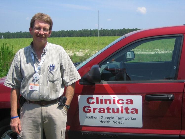 Tom Himelick poses next to his truck that has a sticker on it that reads, "Clinica Gratuita. Southern Georgia Farmworker Health Project."