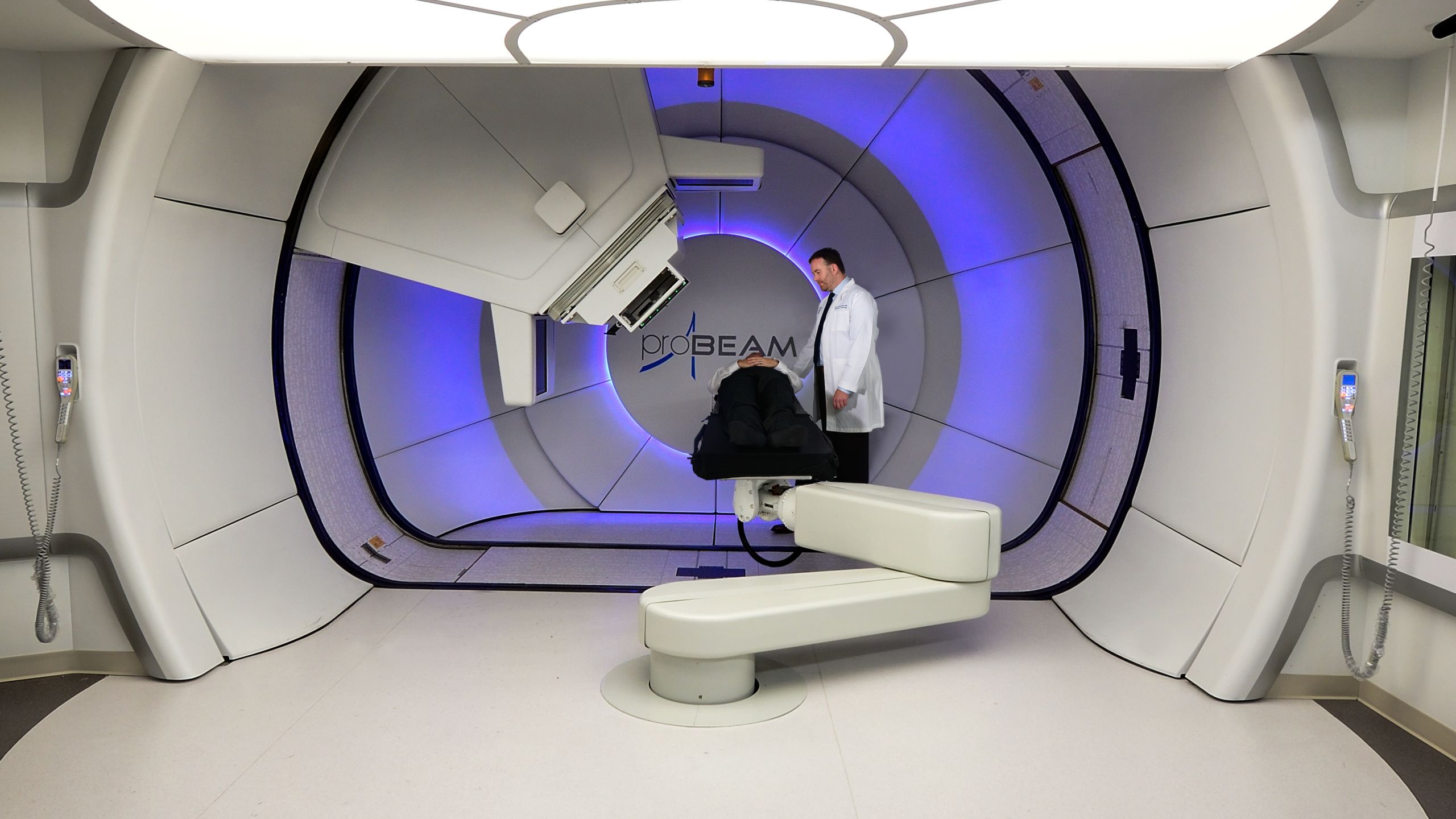 A doctor is standing next to a patient on a treatment table in a very futuristic-looking, circular area where treatment takes place.   