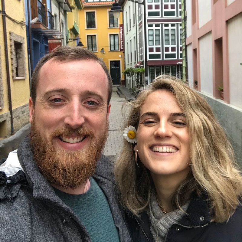 Timothy and Clara Banik smile for a selfie on a Spanish street with colorful buildings in the background.