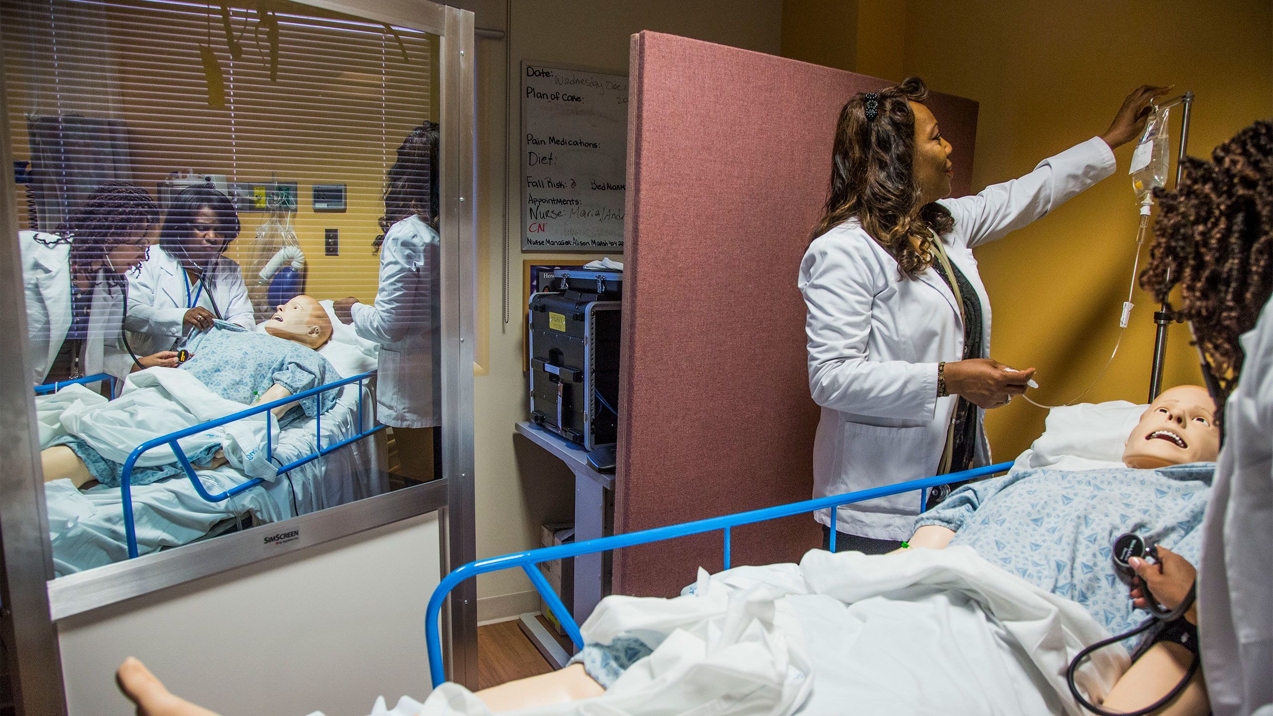 Nurses practice with stethoscopes and IVs in a simulation lab.