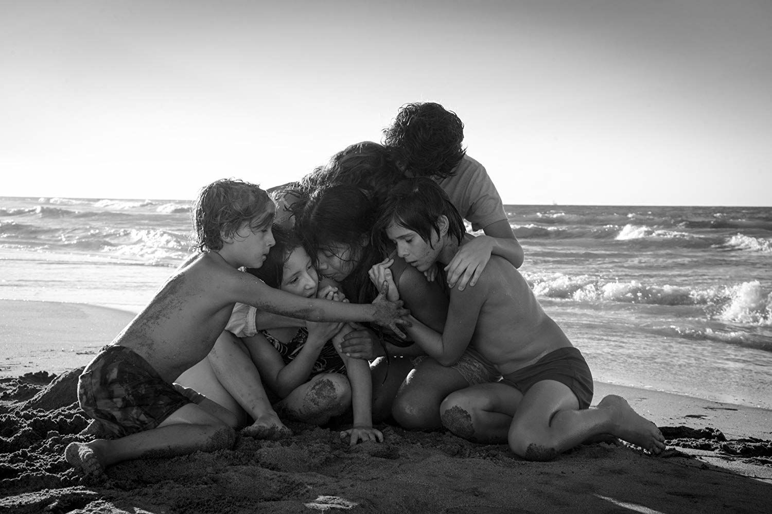 Actors Marina de Tavira, Marco Graf, Yalitza Aparicio, Daniela Demesa, Diego Cortina Autrey, and Carlos Peralta embrace on the beach in a scene from the film "Roma"