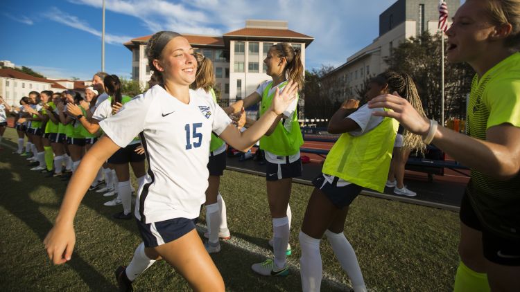 Number 15 of Emory's Women's soccer team high-fives other soccer players